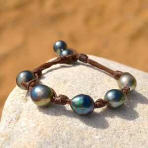Brown leather bracelet with five central baroque Tahitian pearls and two closure pearls displayed on a rock