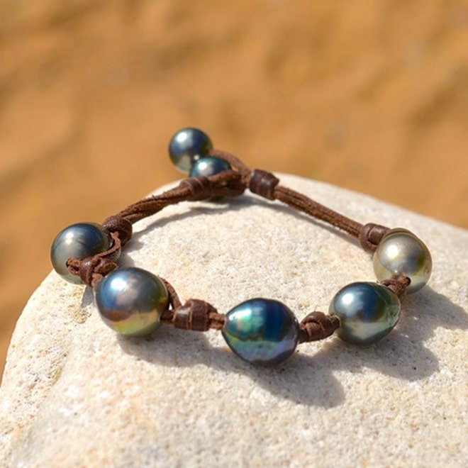 Brown leather bracelet with five central baroque Tahitian pearls and two closure pearls displayed on a rock