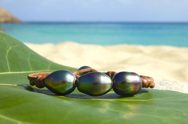 Détail des trois perles semi-baroques de Tahiti sur le bracelet en cuir présenté sur une feuille face à la mer