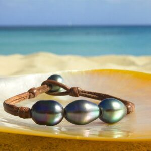 Leather bracelet with three semi-baroque Tahitian pearls displayed on mother-of-pearl by the sea