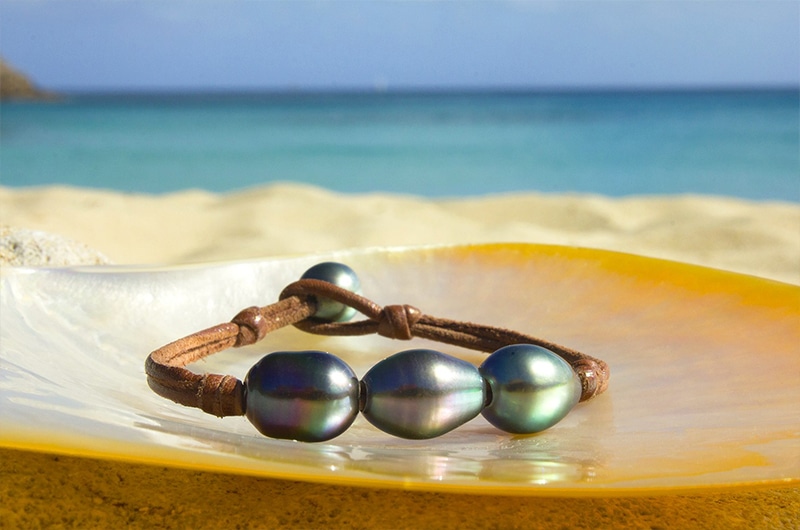 Bracelet en cuir avec trois perles semi-baroques de Tahiti présenté sur une nacre face à la mer