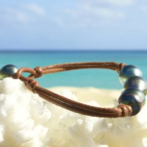Brown leather bracelet with three semi-baroque Tahitian cultured pearls displayed on white coral by the sea