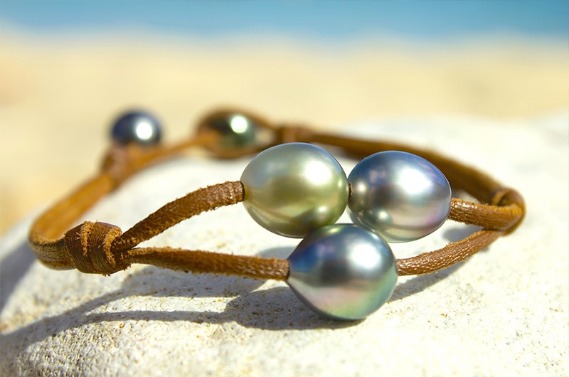 Détail des trois perles de Tahiti sur le bracelet en cuir à deux rangs présenté sur le sable
