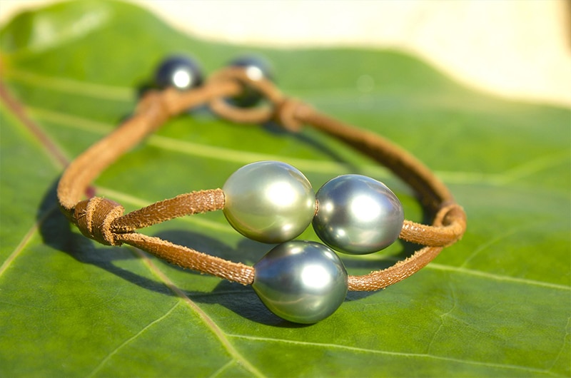 Bracelet en cuir à deux rangs avec trois perles de Tahiti présenté sur une feuille verte
