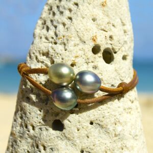 Brown two-strand leather bracelet with three Tahitian cultured pearls displayed on a rock by the sea