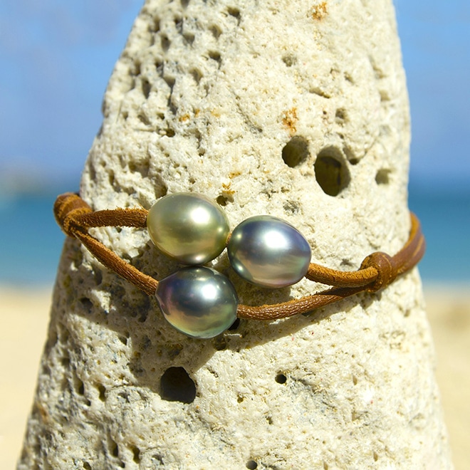 Bracelet en cuir marron à deux rangs avec trois perles de culture de Tahiti présenté sur une roche face à la mer