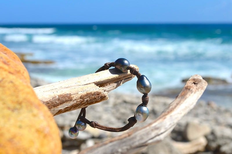 Leather bracelet with three 11.5 mm Tahitian pearls and knots displayed on wood by the sea