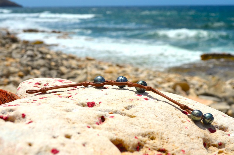 Bracelet with three 11 mm circled Tahitian pearls, knots and two closure pearls displayed on a rock by the sea