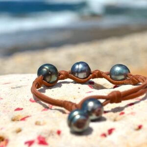 Full view of the leather bracelet with three 11 mm circled Tahitian pearls and knots displayed on a rock by the sea