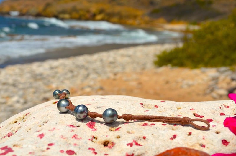 Leather bracelet with three 11 mm circled Tahitian pearls and knots displayed on a rock at the beach