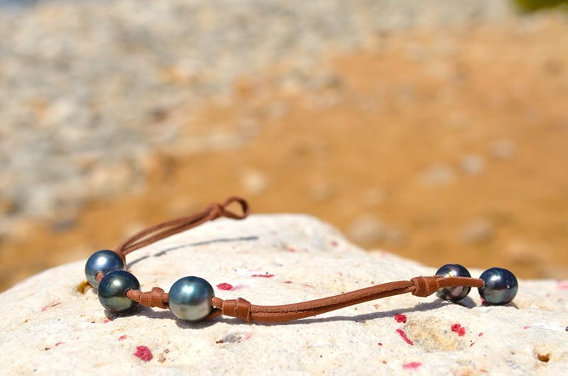 Leather bracelet with three 9.5 mm Tahitian pearls and knots displayed on a rock at the beach