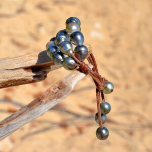 Side view of the three-strand bracelet with twenty baroque Tahitian pearls showing the leather and closure pearls against sand