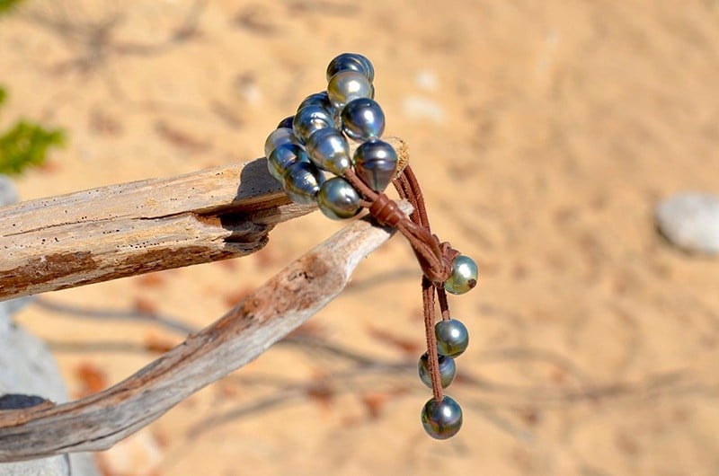 Vue latérale du bracelet à trois rangs avec vingt perles baroques de Tahiti montrant le cuir et les perles de fermeture sur fond de sable