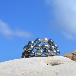 Three-strand bracelet with twenty baroque Tahitian pearls displayed from the front on a rock under a blue sky