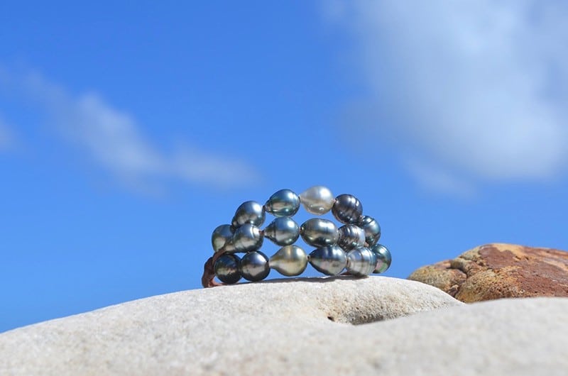 Bracelet à trois rangs avec vingt perles baroques de Tahiti présenté de face sur une roche sous un ciel bleu