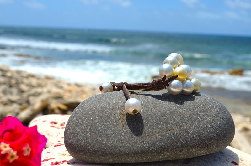 Détail du montage en cuir et des perles de fermeture du bracelet à trois rangs présenté sur une roche face à la mer