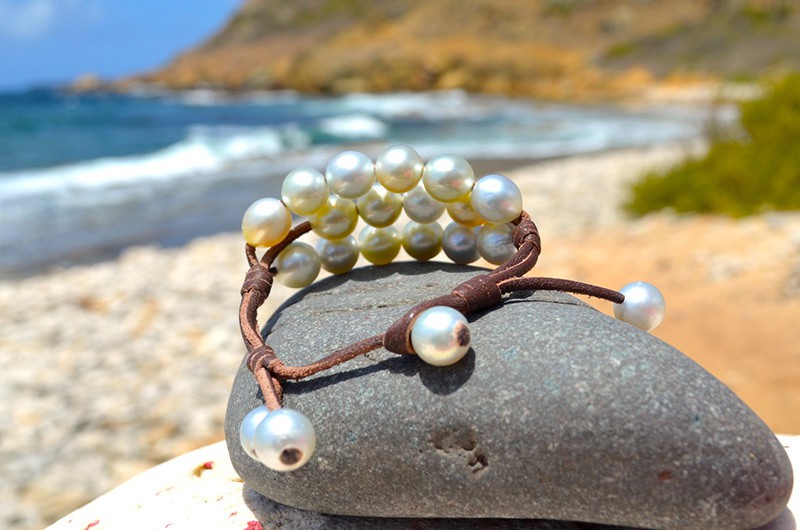 Bracelet à trois rangs avec vingt perles blanches d’Australie présenté sur une roche au bord de mer