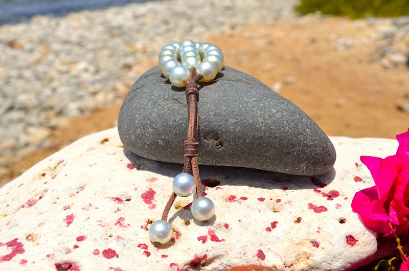 Vue complète du bracelet à trois rangs avec vingt perles blanches d’Australie présenté sur une roche avec des fleurs roses