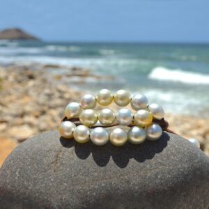 Brown leather three-strand bracelet with twenty white Australian cultured pearls displayed on a rock by the sea