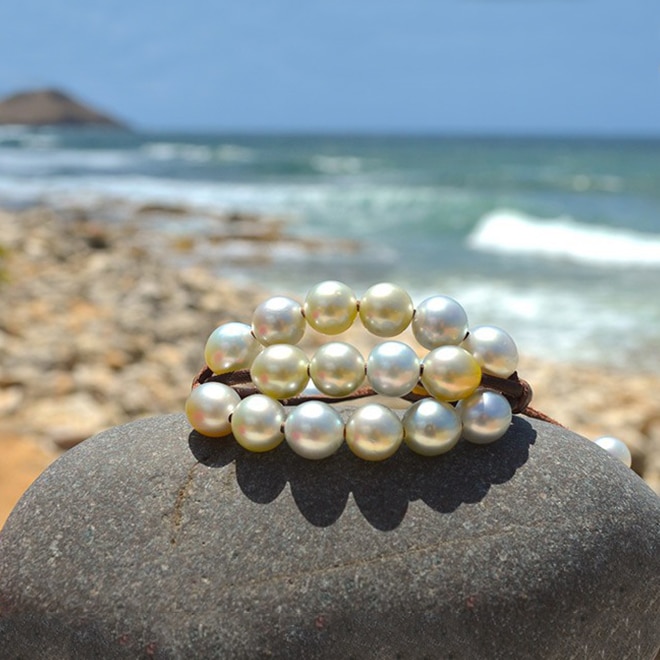 Bracelet en cuir marron à trois rangs avec vingt perles blanches de culture d’Australie présenté sur une roche face à la mer