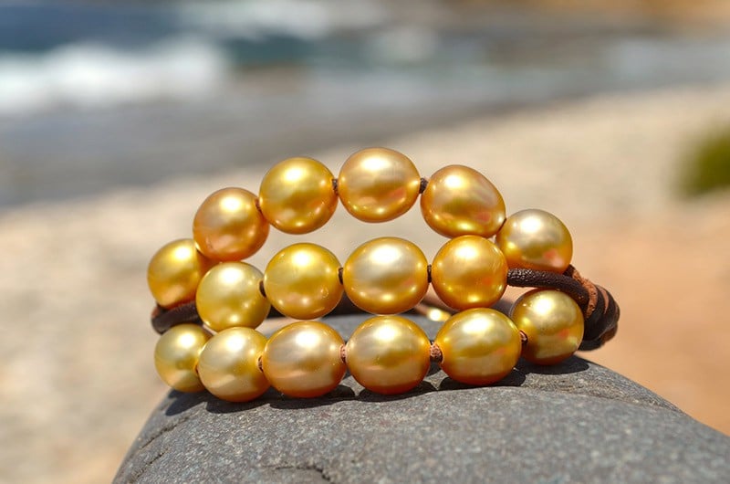 Détail des vingt perles dorées d’Australie et du montage à trois rangs du bracelet présenté sur une roche