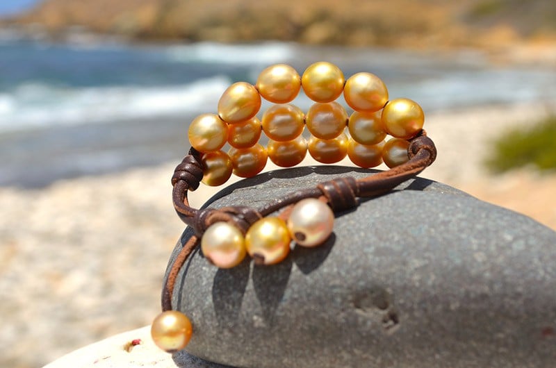Bracelet à trois rangs avec vingt perles dorées d’Australie présenté sur une roche face à la mer