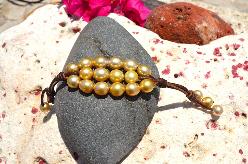 Vue complète du bracelet à trois rangs avec vingt perles dorées d’Australie présenté sur une roche avec des fleurs roses