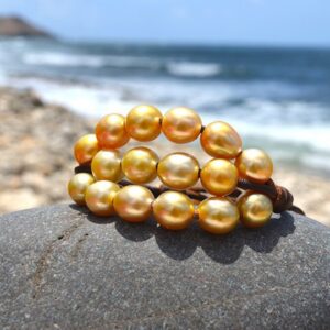 Brown leather three-strand bracelet with twenty golden Australian cultured pearls displayed on a rock by the sea