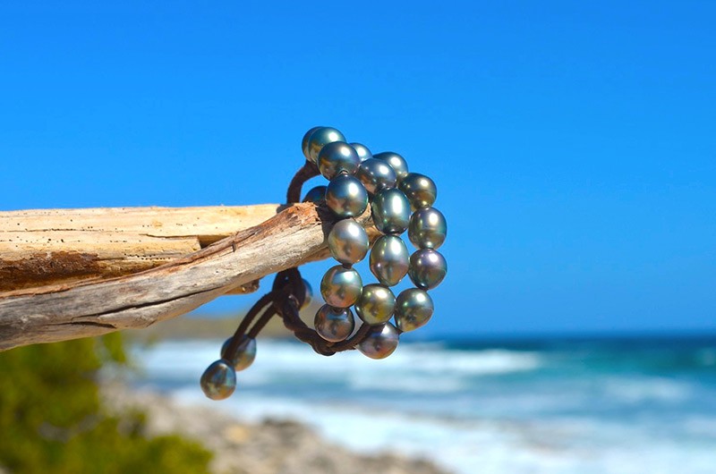 Vue complète du bracelet à trois rangs avec vingt perles semi-baroques de Tahiti présenté sur du bois face à la mer