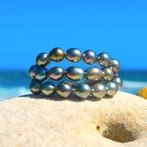 Brown leather three-strand bracelet with twenty semi-baroque Tahitian pearls displayed on coral by the sea