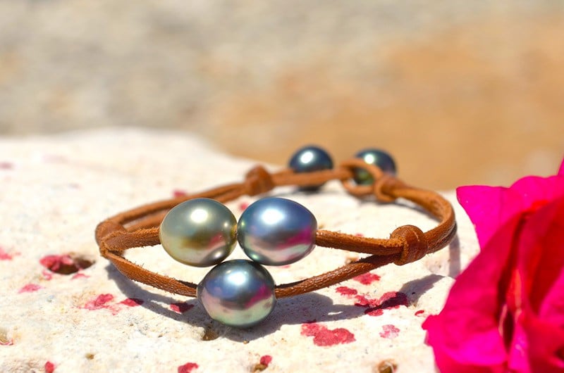 Bracelet en cuir à deux rangs avec trois perles semi-baroques de Tahiti présenté sur du corail avec des fleurs roses