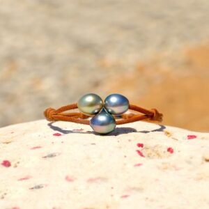 Brown leather two-strand bracelet with three semi-baroque Tahitian pearls displayed on a rock