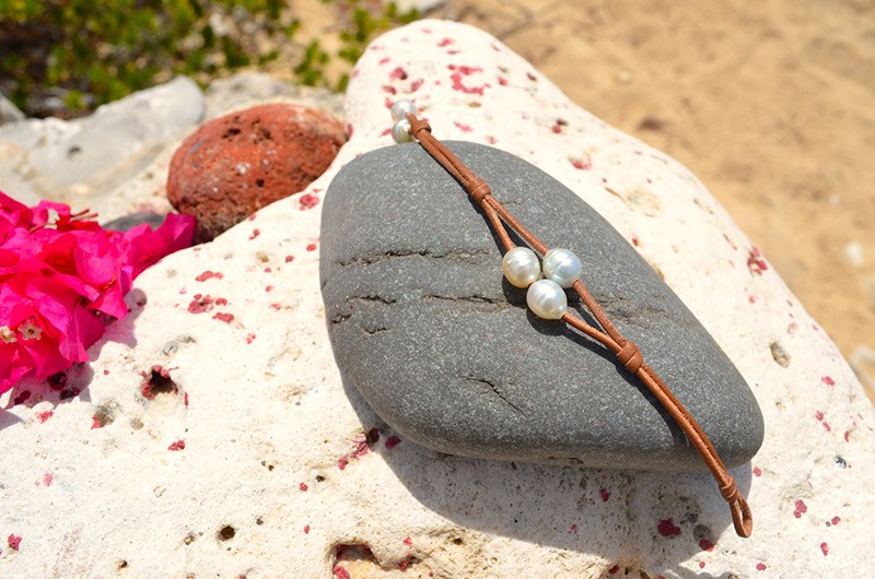 Détail des trois perles blanches d’Australie et du montage en cuir à deux rangs présenté sur du corail avec des fleurs roses