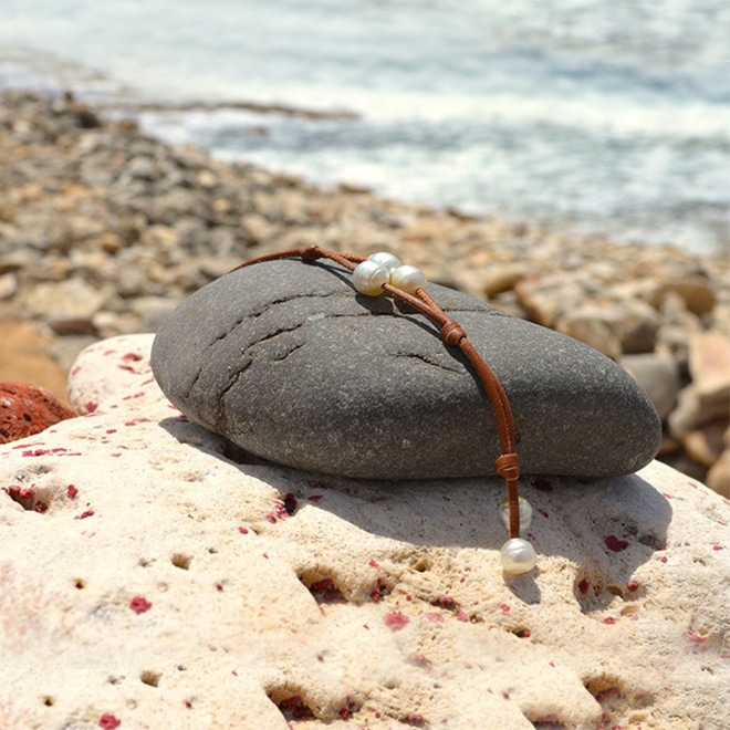 Vue arrière du bracelet en cuir à deux rangs avec trois perles blanches d’Australie présenté sur une roche au bord de mer