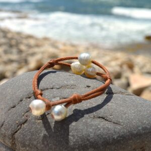 Full view of the two-strand bracelet with three white Australian pearls displayed on a rock by the sea