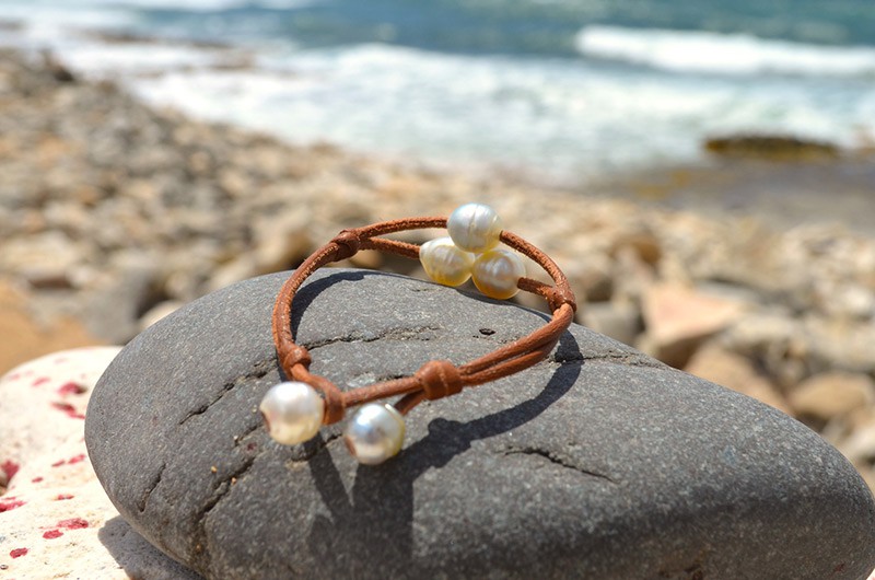Vue complète du bracelet à deux rangs avec trois perles blanches d’Australie présenté sur une roche face à la mer