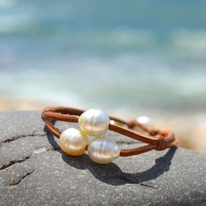 Brown leather two-strand bracelet with three white Australian cultured pearls displayed on a rock by the sea
