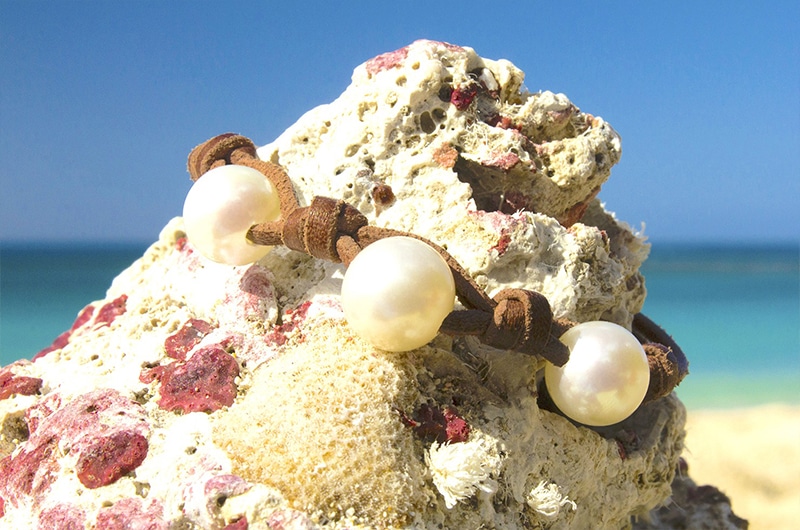 Détail des trois perles blanches d’eau douce et du montage en cuir présenté sur du corail face à la mer