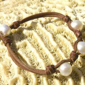 Vue complète du bracelet en cuir avec trois perles blanches d’eau douce présenté sur du corail