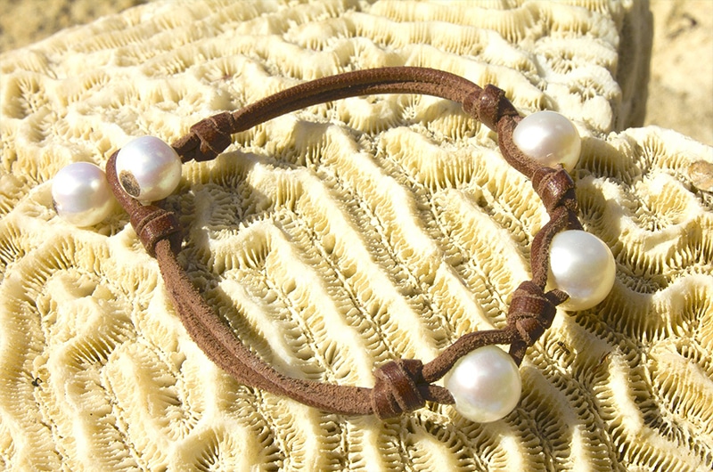 Vue complète du bracelet en cuir avec trois perles blanches d’eau douce présenté sur du corail