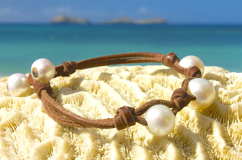 Bracelet en cuir marron avec trois perles blanches de culture d’eau douce présenté en vue complète sur du corail face à la mer