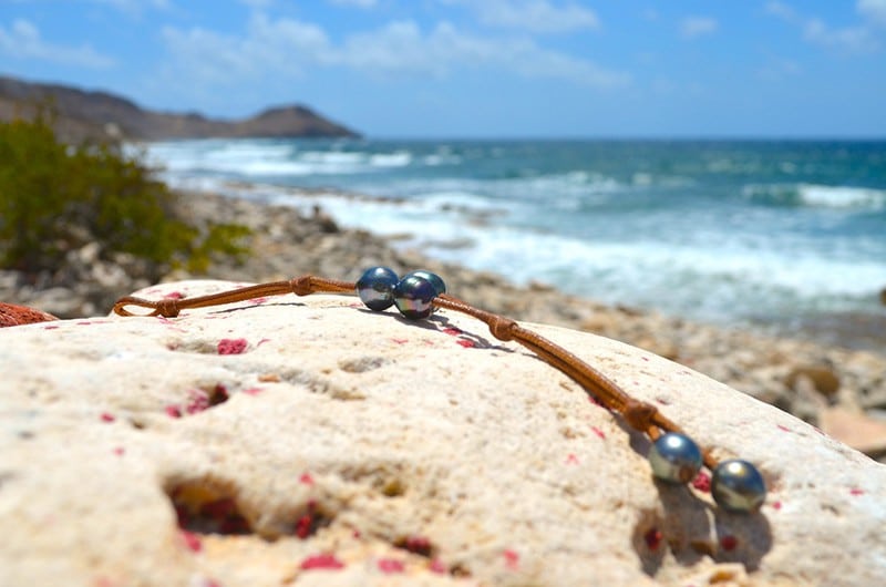 Bracelet en cuir à deux rangs avec trois perles baroques de Tahiti présenté sur du bois face à la mer
