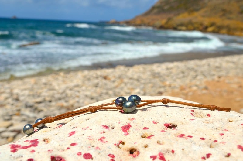 Vue complète du bracelet à deux rangs avec trois perles baroques de Tahiti présenté sur du corail face à la mer