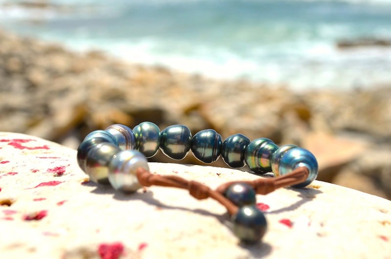 Single-strand bracelet with twelve 11.5 mm Tahitian pearls displayed on coral by the sea
