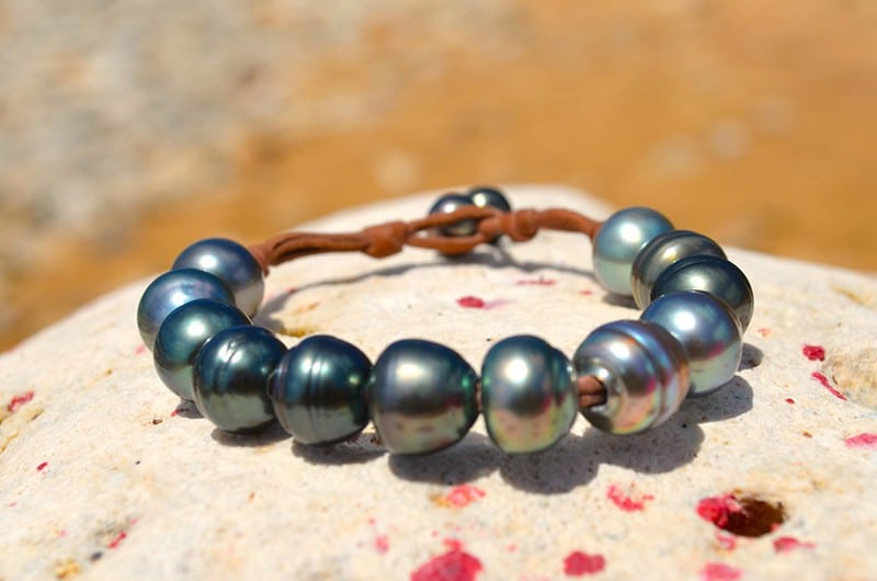 Close-up of the twelve 11.5 mm Tahitian pearls and leather bracelet setting displayed on coral