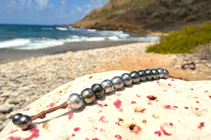 Full view of the single-strand leather bracelet with twelve 11.5 mm Tahitian pearls displayed by the sea