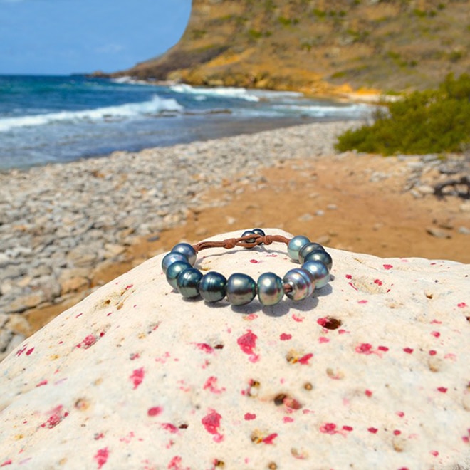 Brown leather single-strand bracelet with twelve 11.5 mm Tahitian cultured pearls displayed on coral by the sea