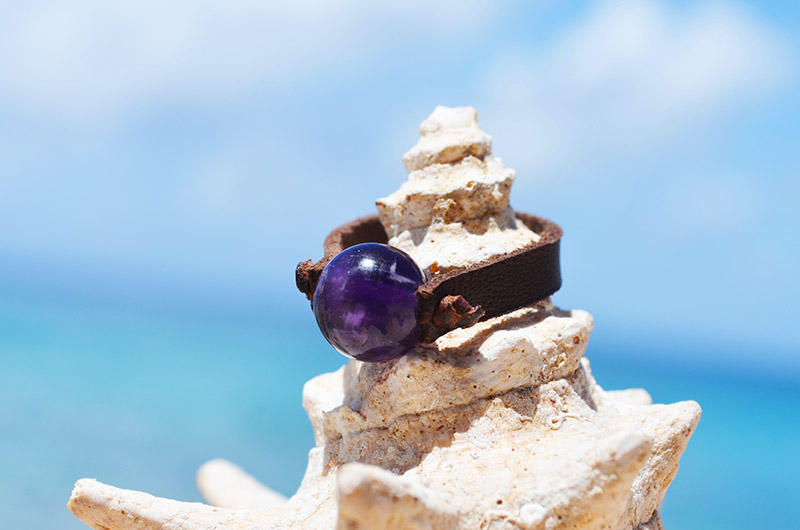 Bague en cuir marron avec améthyste ronde de 10 mm présentée sur un coquillage face à la mer