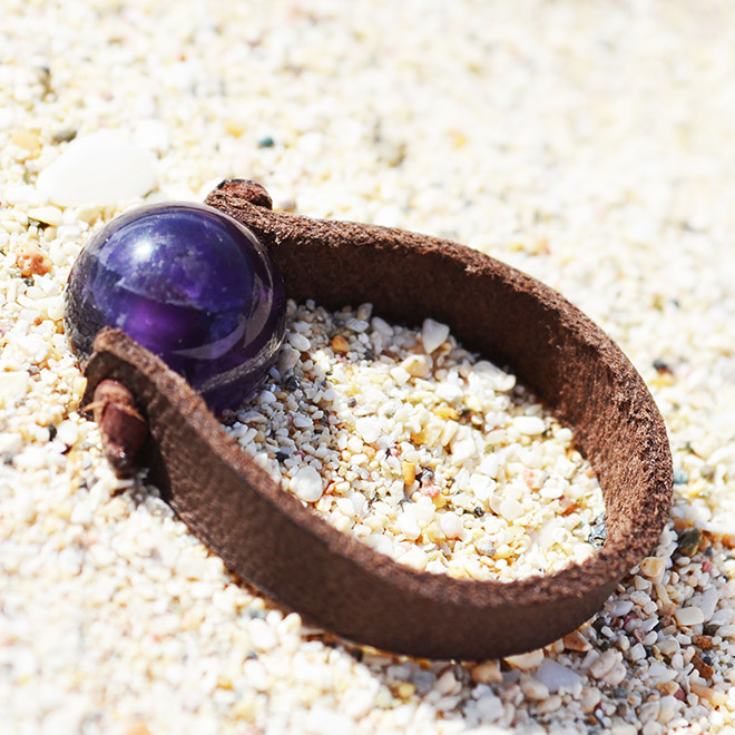 Bague en cuir marron avec améthyste ronde de 10 mm présentée sur du sable