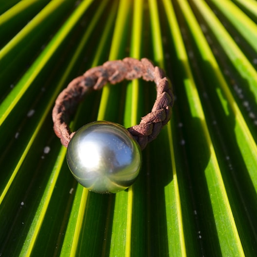 Braided brown leather ring with one Tahitian cultured pearl, displayed on a palm leaf